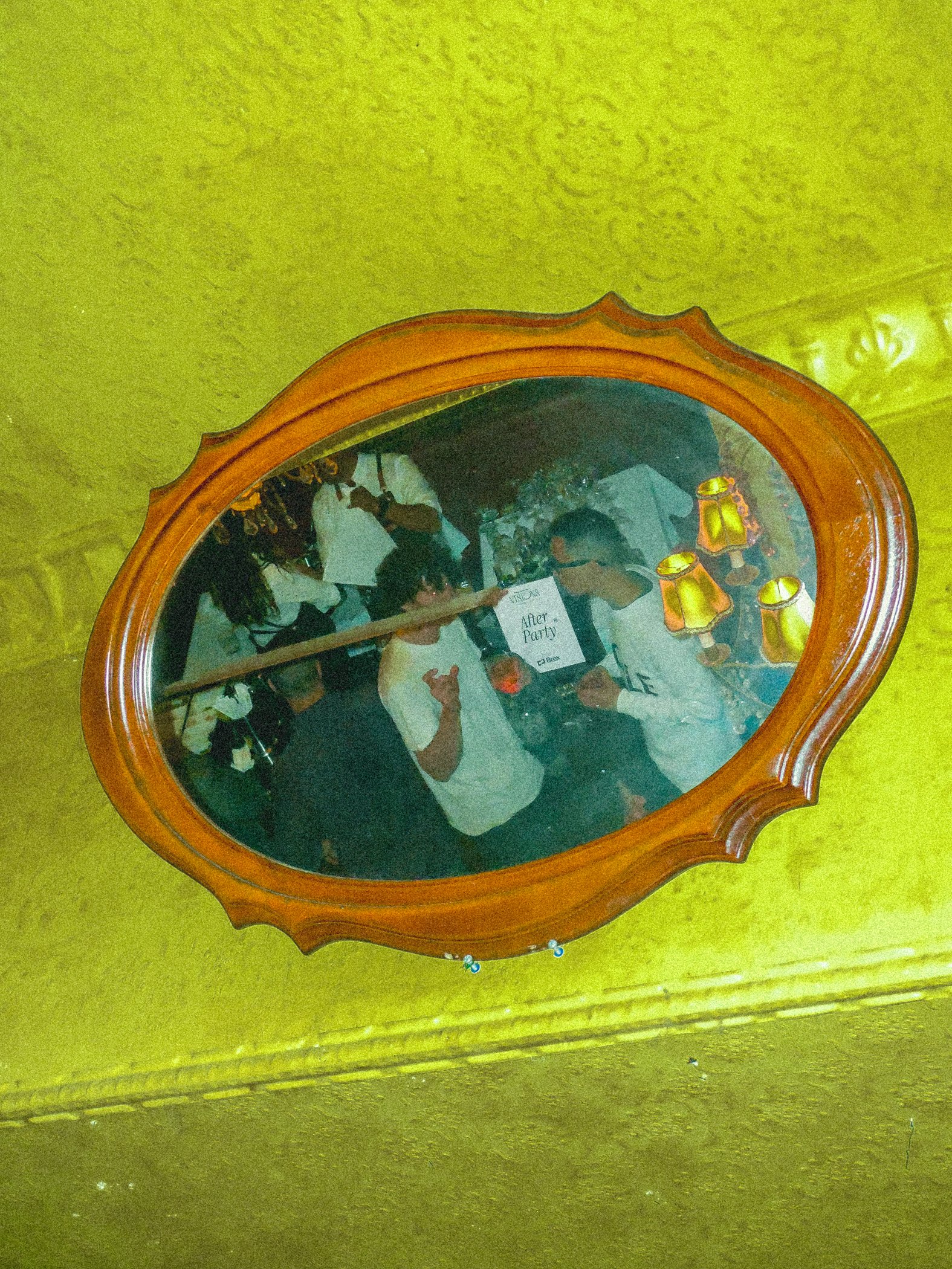 An ornate mirror on a chartreuse wall reflects guests and a VISIONS After Party sign